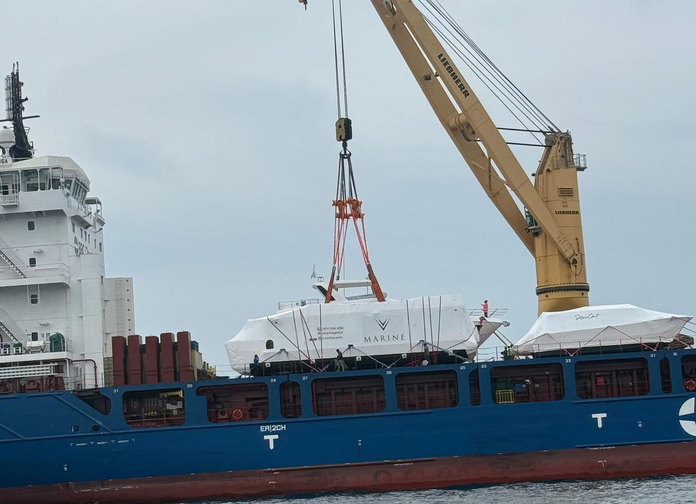 A wrapped V-Marine hull lifted onto a cargo ship's deck by the ship's crane