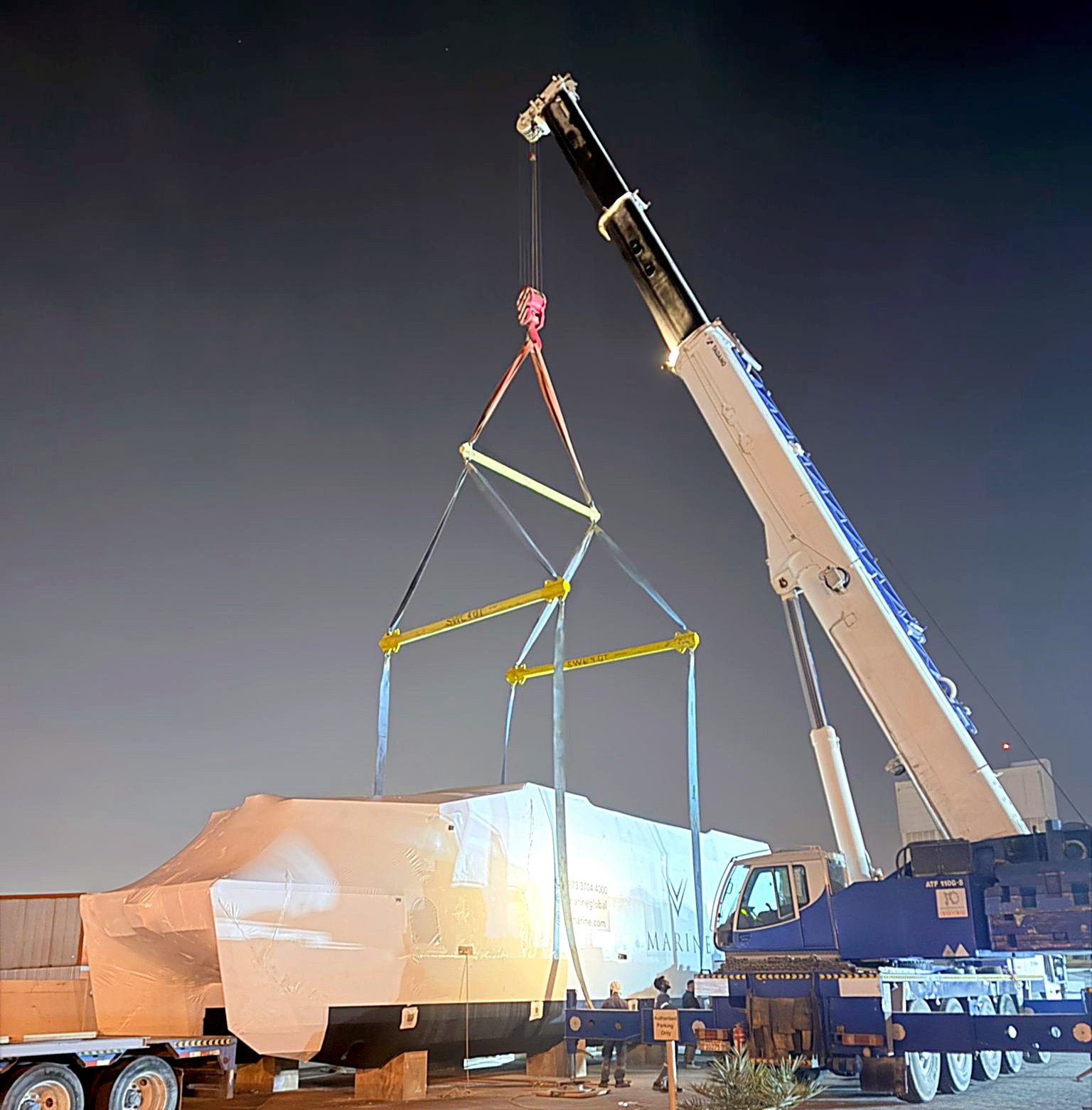 A crane lifting a wrapped V-Marine hull from the shipyard at night